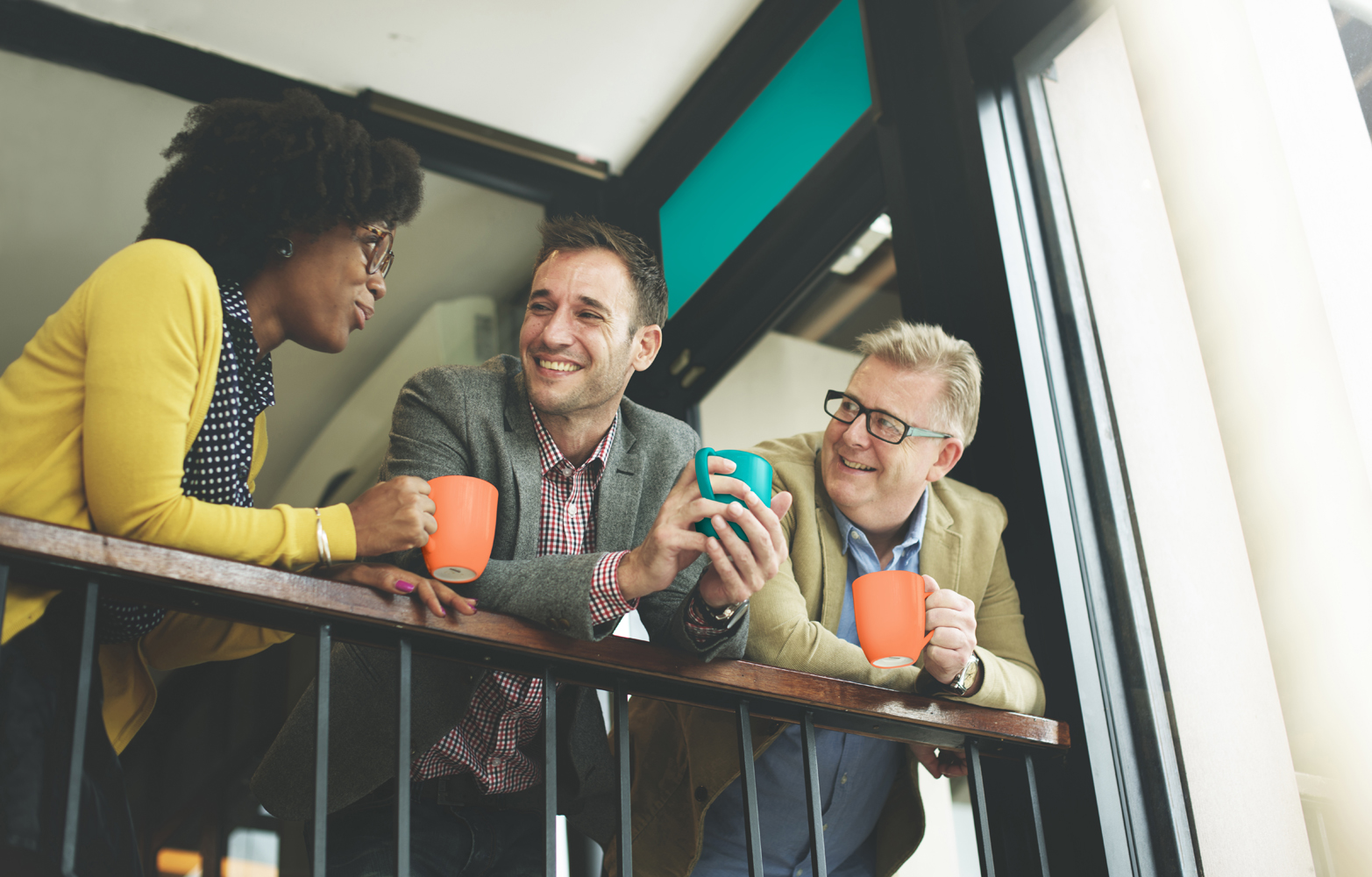 3 colleagues leaning on stairwell railing drinking from cups and smiling