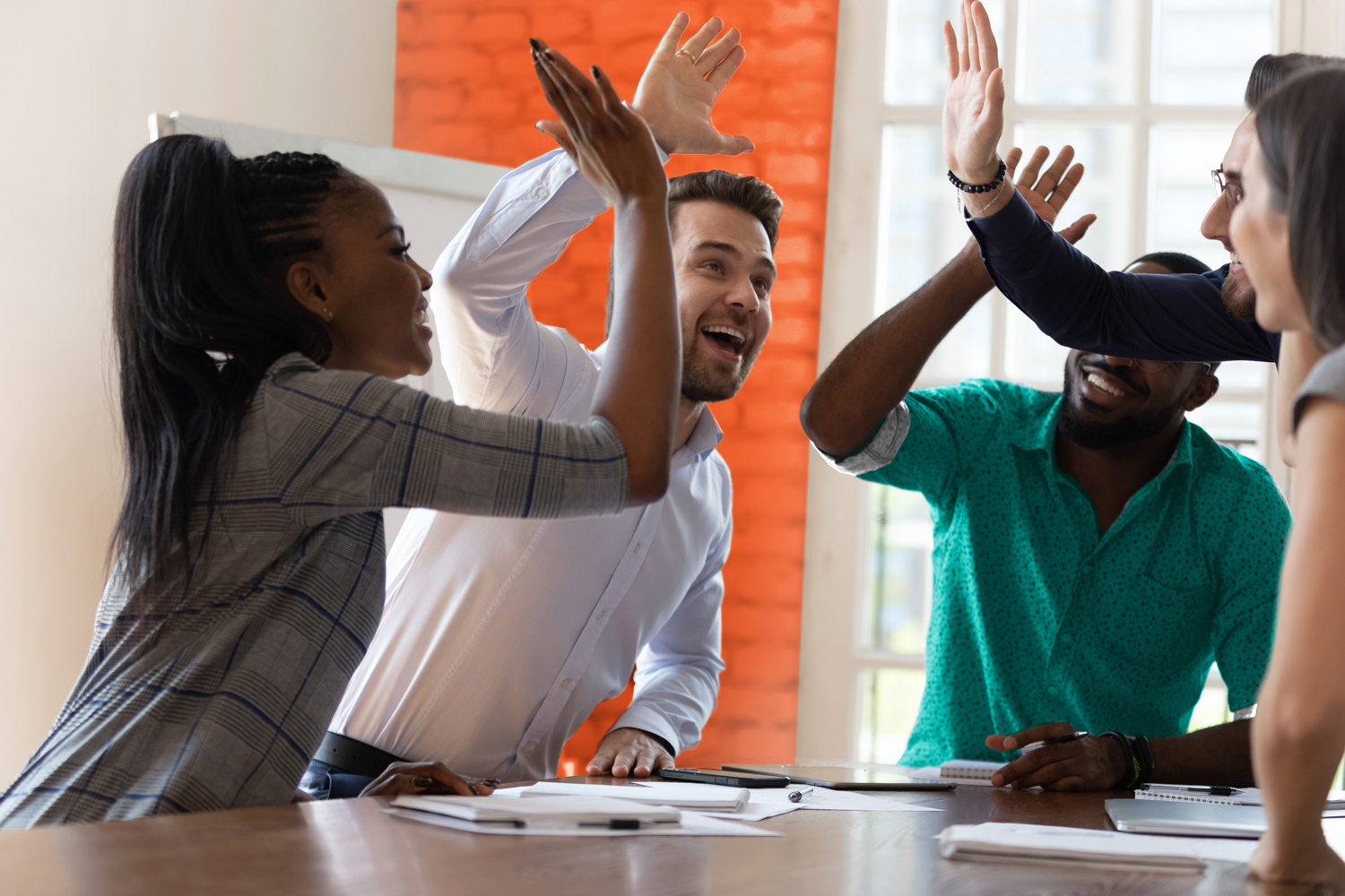 Multiracial euphoric business team people give high five at office table, happy excited diverse work group engaged in teambuilding celebrate corporate success win partnership power teamwork concept
