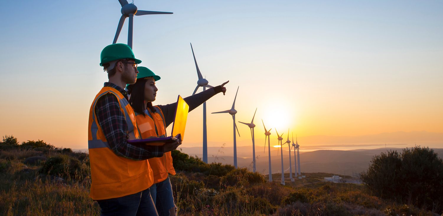 Young maintenance engineer team working in wind turbine farm at sunset