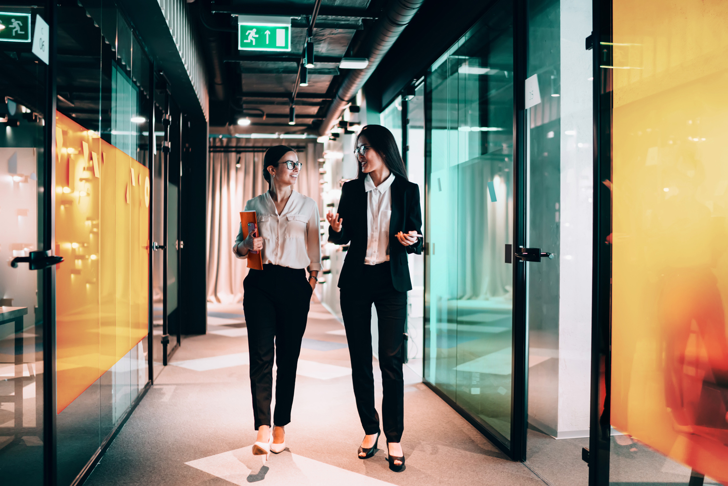 Confident Caucasian colleagues 30s enjoying friendship relations in office workspace, successful female executive managers walking in corporate hallway and discussing business ideas for cooperate