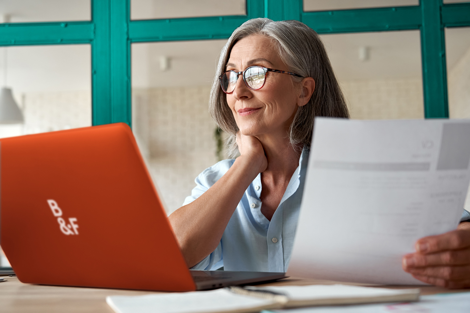 Smiling mature middle aged business woman using laptop working on computer sitting at desk. Happy old businesswoman hr holding cv interviewing distance applicant, senior seeker searching job online.