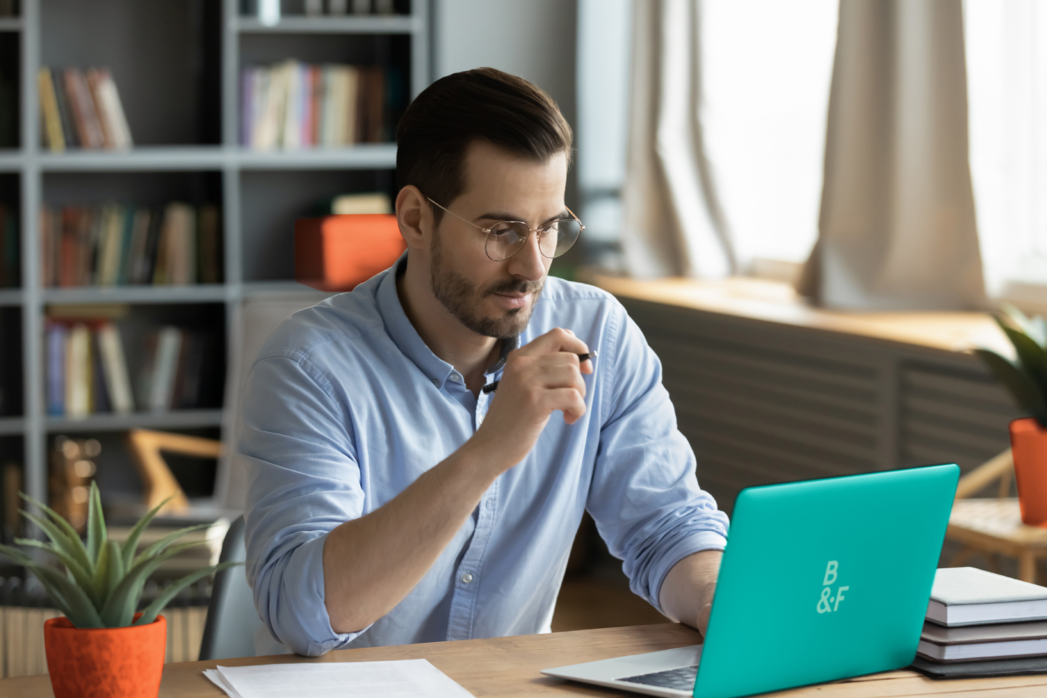 Concentrated young businessman in eyewear looking at laptop screen, web surfing information in internet or working distantly online at home office, communication remotely with client or study.