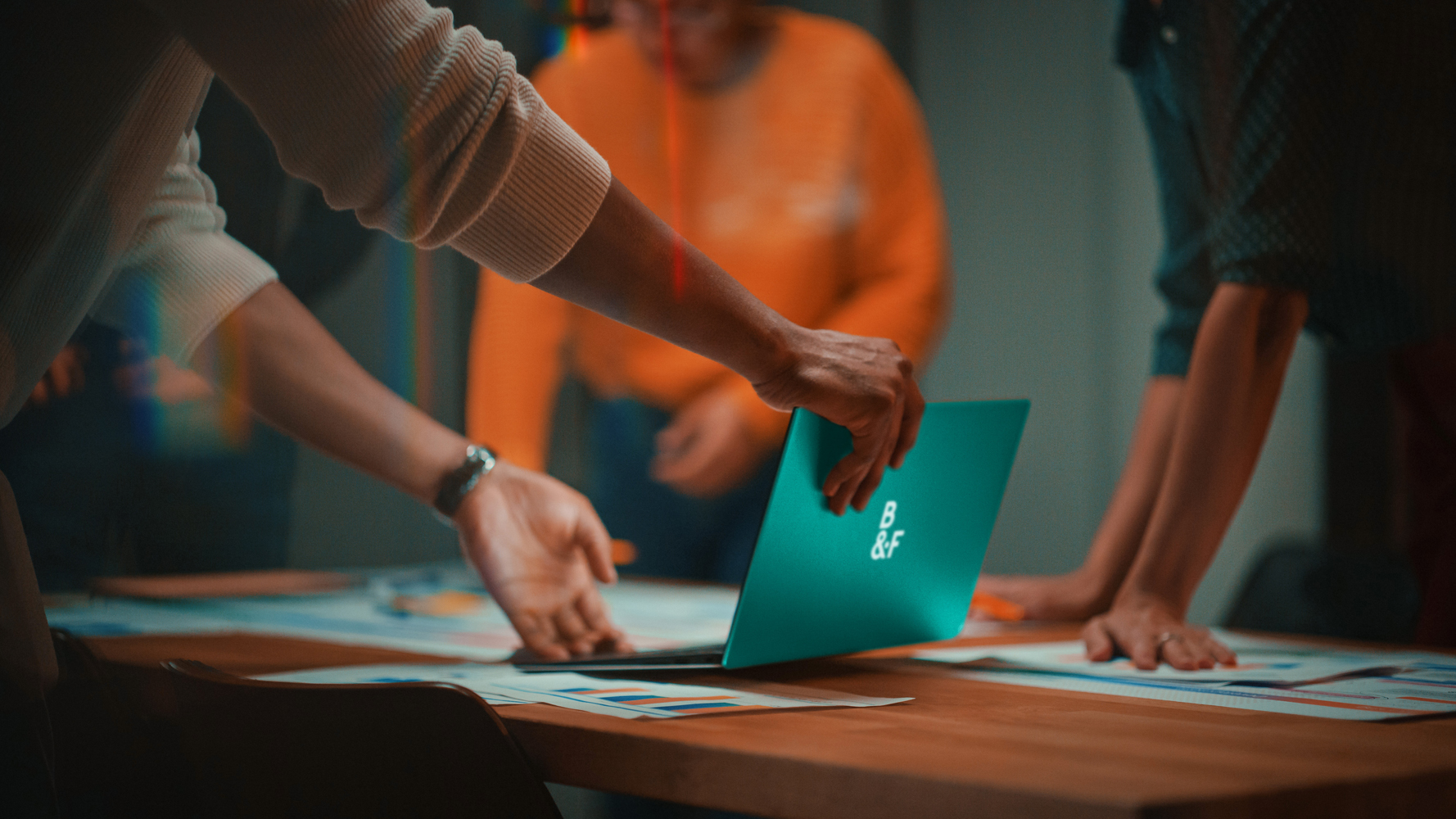 Close Up of Diverse Multiethnic Team Having Conversation in Meeting Room in a Creative Office. Colleagues Lean On a Conference Table, Look at Laptop Computer and Make Notes with Pencils on Notebooks.